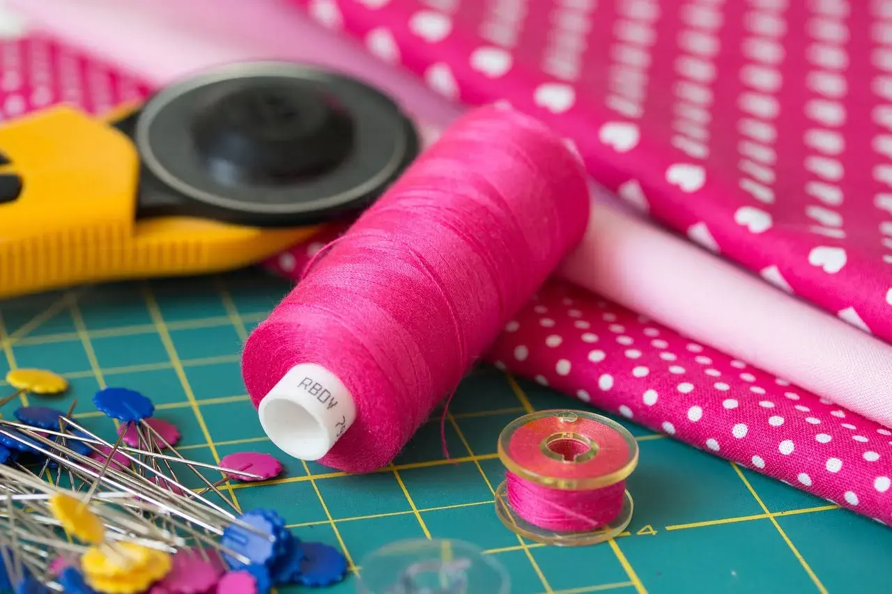 Różowe nici, szpilki, rolka do tkanin i materiały z wzorami – idealny zestaw do szycia z tkaniny **non woven**.