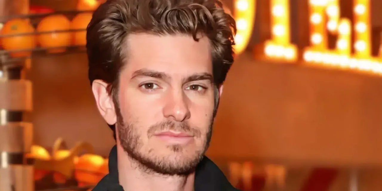 Andrew Garfield, avec une barbe naissante, pose devant des lumières chaudes. On spécule sur son prochain film.