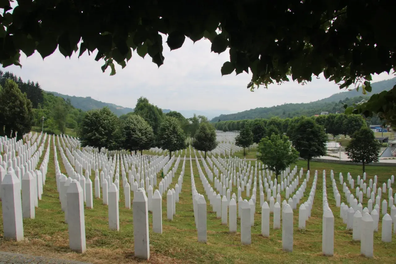 Enormt fält med vita gravstenar, en påminnelse om folkmordet i Srebrenica. Grönskande kullar i bakgrunden.