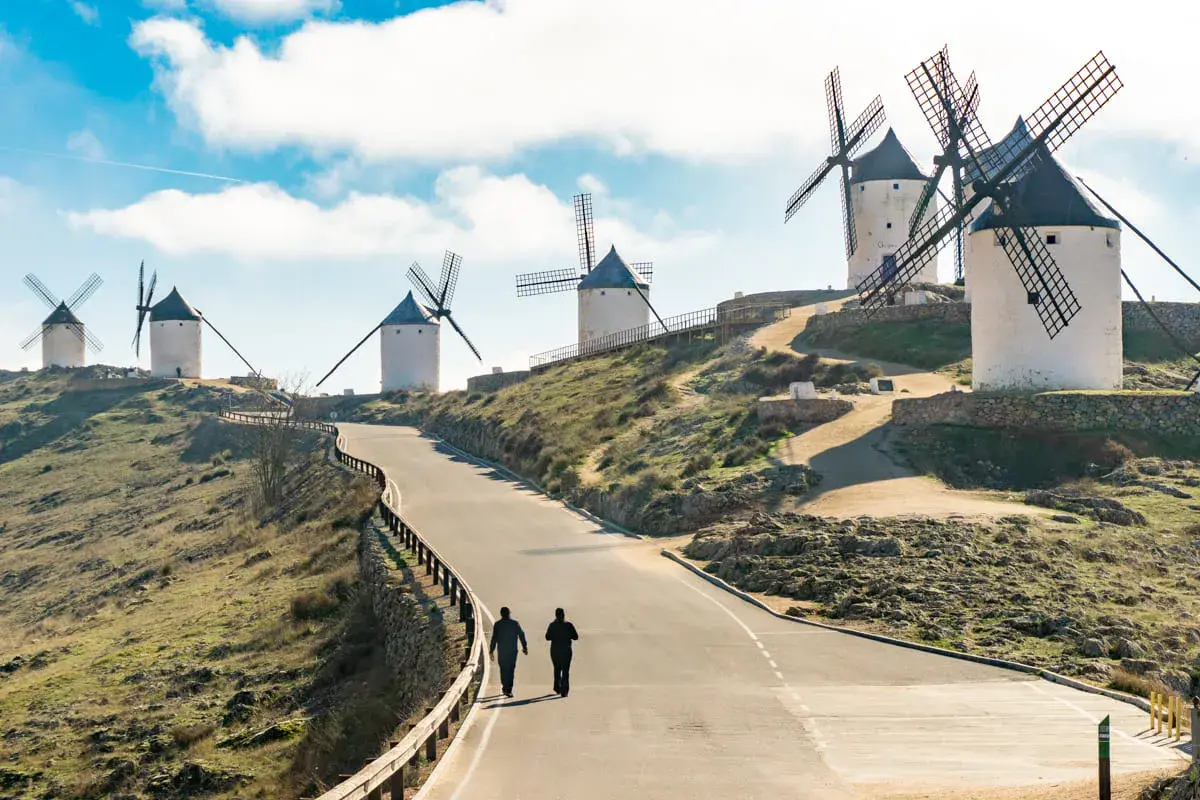 Molinos de viento en la ruta de Don Quijote, con dos personas caminando por un camino.
