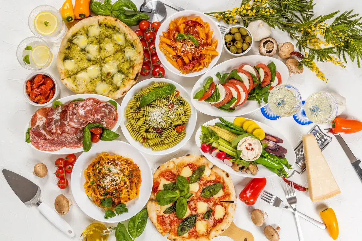 Obfity tradycyjny włoski obiad: pizze, makarony, sałatka caprese, wędliny, warzywa i ser.
