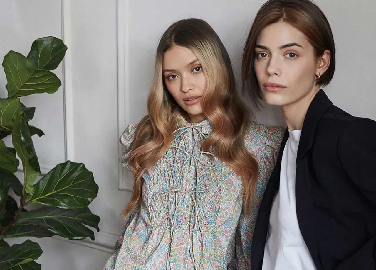 Due modelle con capelli biondi e castani, una con abito floreale, l'altra con blazer. L'armocromia inverno capelli valorizza i loro toni.