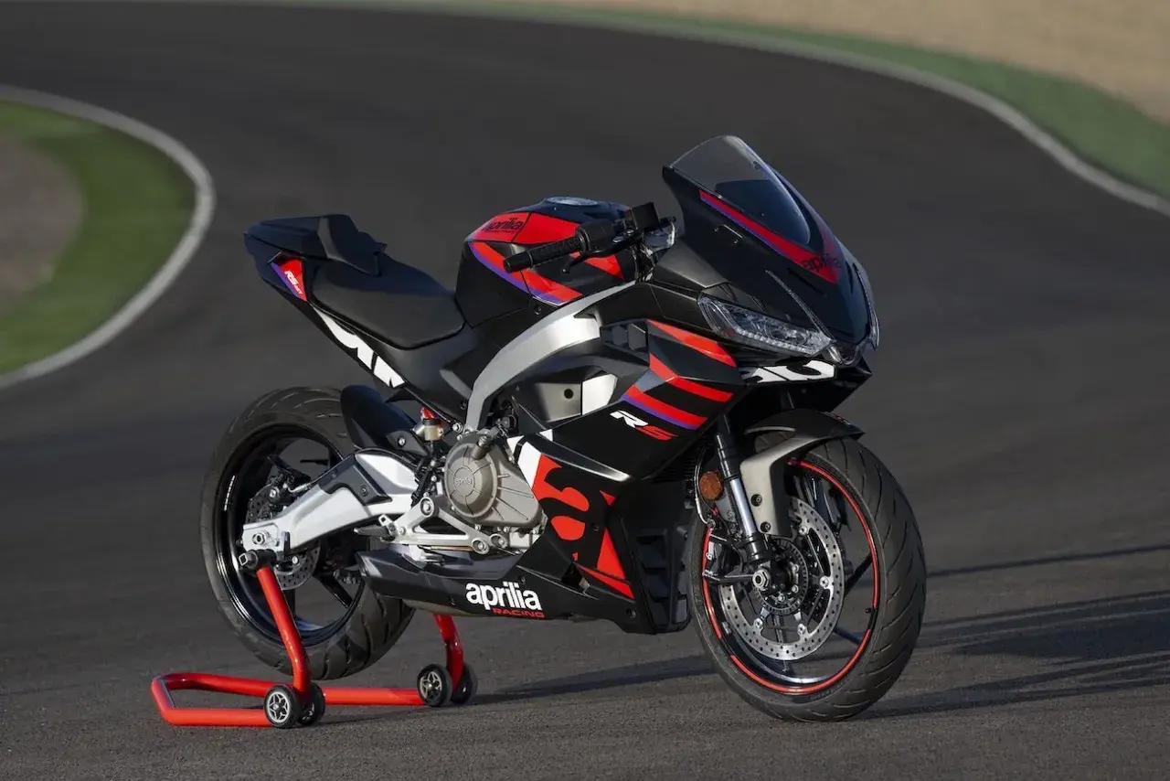 Czarny motocykl sportowy Aprilia na czerwonym stojaku na torze wyścigowym.