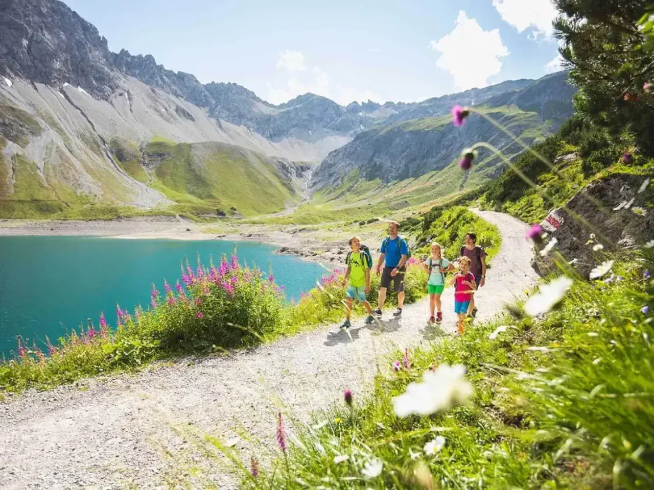 Familie genießt eine Wanderung im Brandnertal. Türkiser Bergsee, grüne Hänge und blühende Wiesen.
