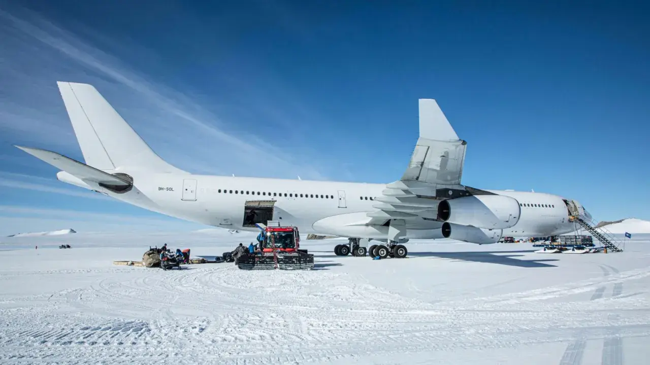 Biały airbus a340-300 na śniegu, z obsługą naziemną i ratrakiem.