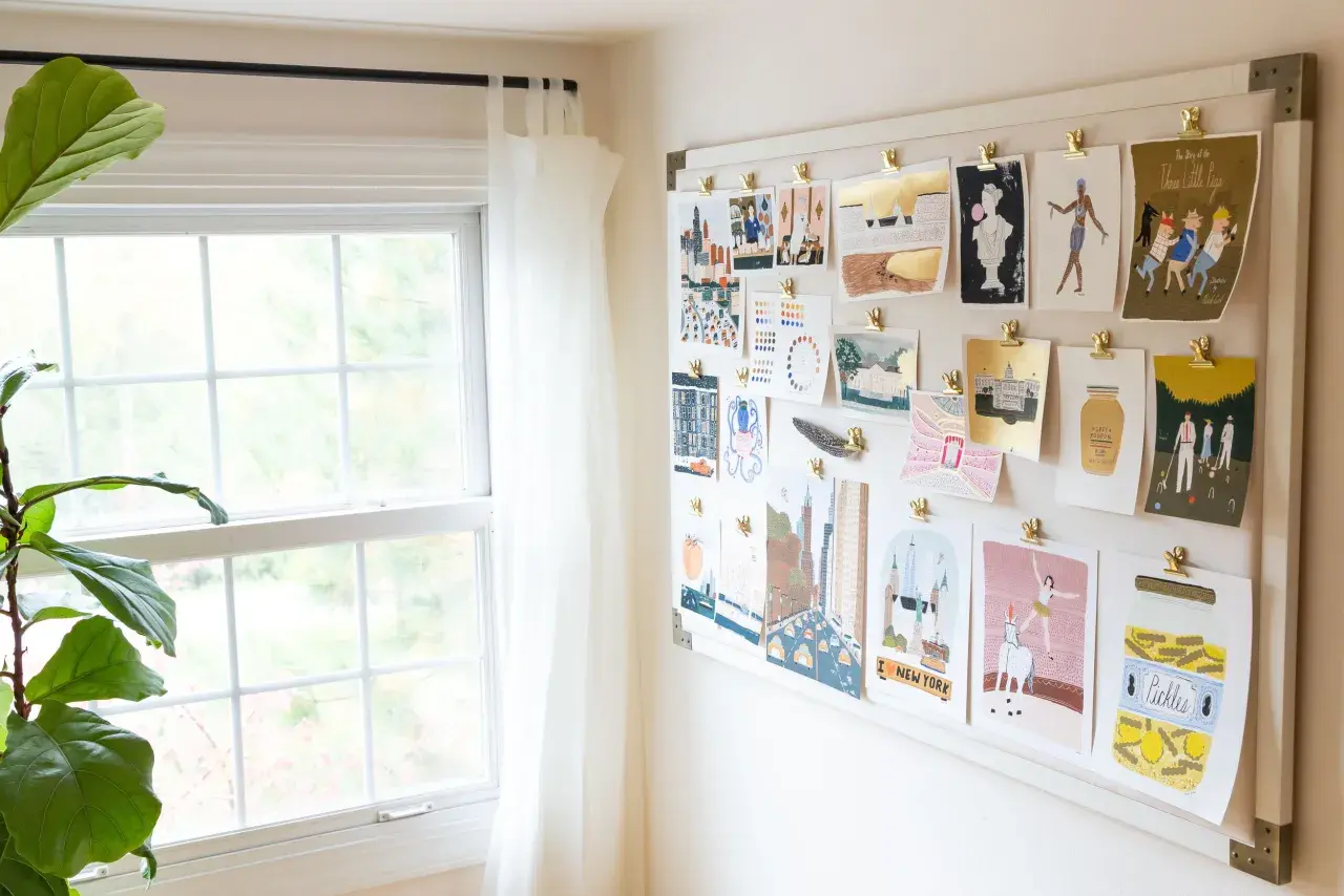 A mood board displays a collection of minimalist contemporary art prints, featuring cityscapes, figures, and whimsical illustrations, all clipped to a white board.