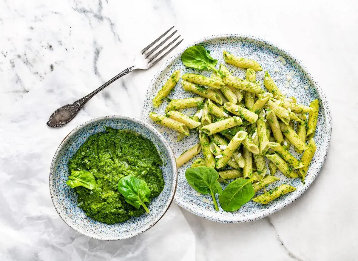 Penne z domowym pesto ze szpinaku, podane w miseczce i na talerzu, z widelcem obok.