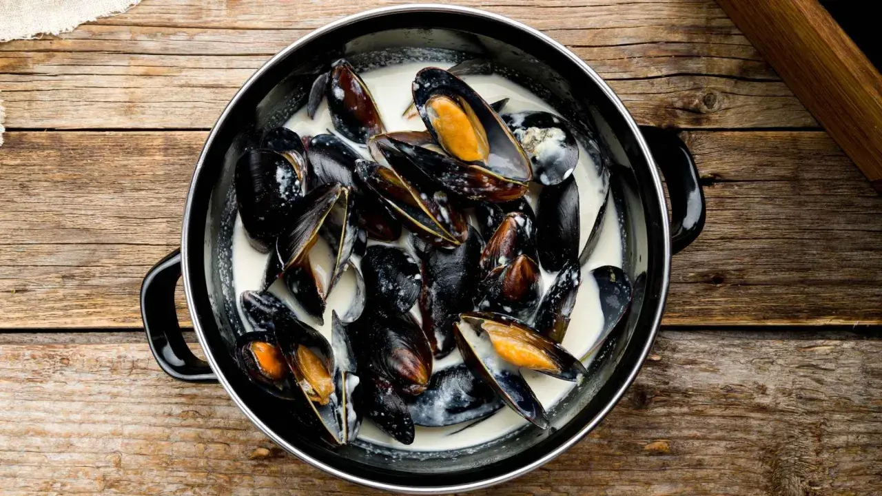 Un plat de moules à la crème, prêtes à être dégustées sur une table en bois rustique.