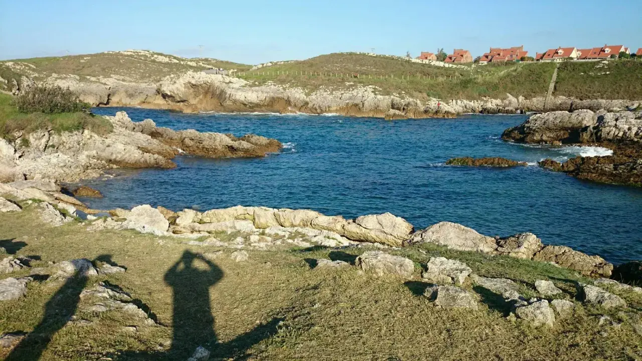 La **playa de Canallave** se asoma entre rocas y aguas turquesas. En la colina, casas de tejados rojos vigilan el mar.
