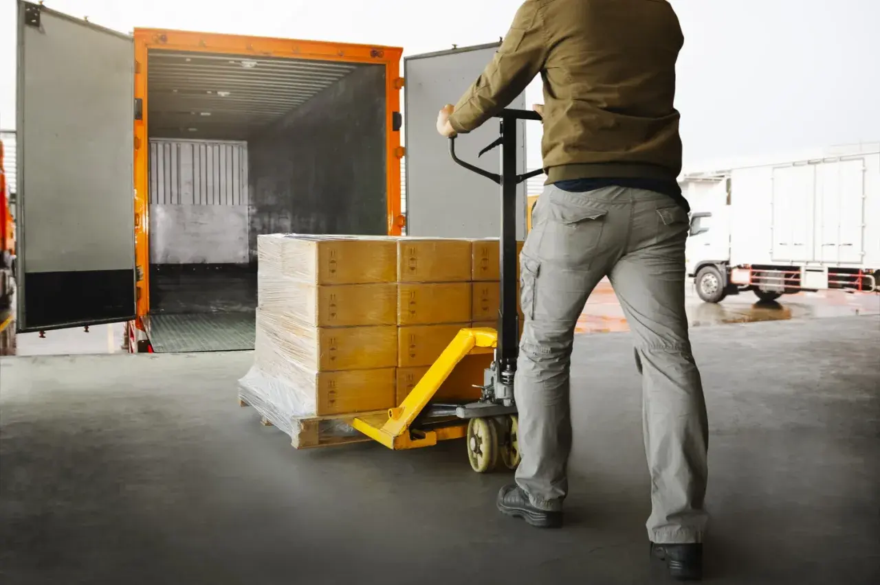 Pracownik magazynu przemieszcza paletę z paczkami za pomocą wózka widłowego, przygotowując towar do **cross trade** transportu.