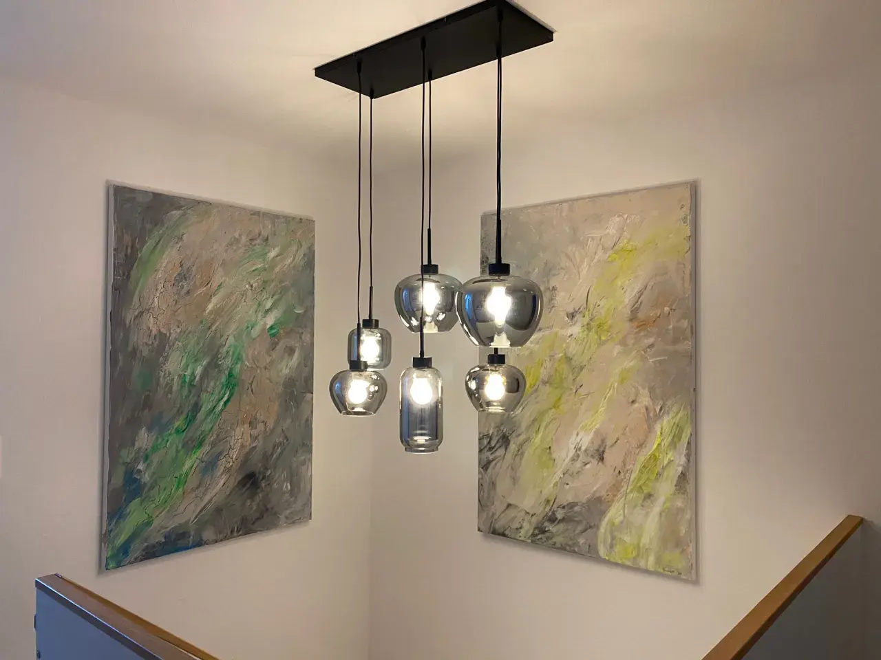 Moderne Hängelampen montieren über einem Treppenaufgang, flankiert von abstrakter Kunst.