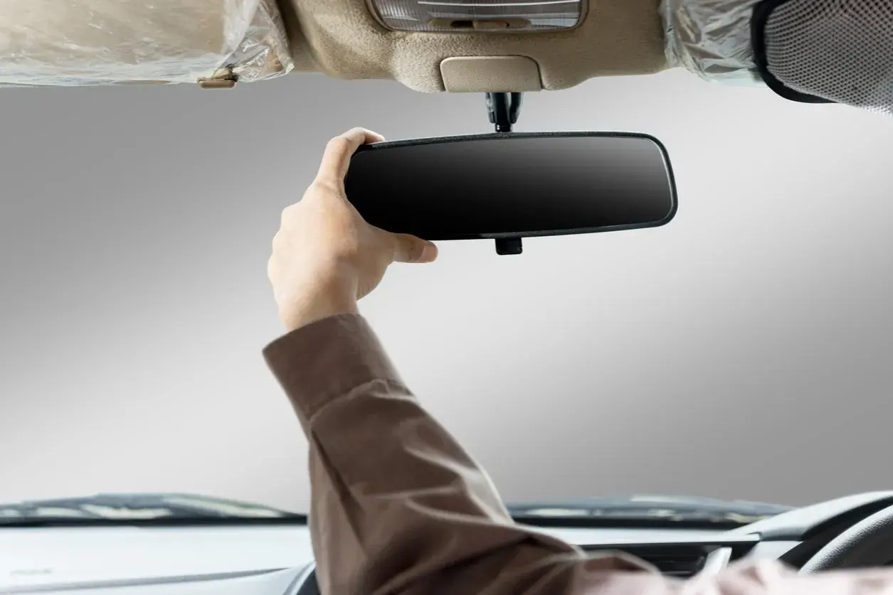 Main d'un conducteur ajustant le rétroviseur intérieur de sa voiture. Apprenez comment emboîter un rétroviseur intérieur pour une meilleure visibilité.