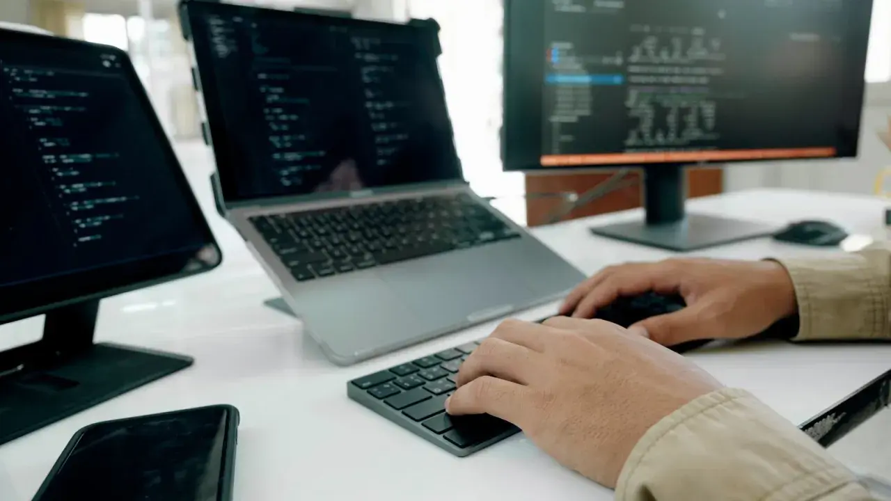 Programista pracuje nad nowym oprogramowaniem użytkowym, pisząc kod na laptopie i monitorze.