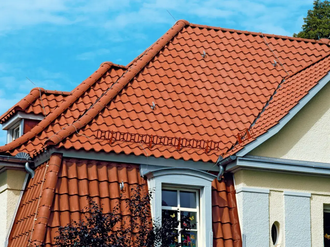 Dwa rodzaje dachów z czerwonej dachówki ceramicznej, jeden płaski, drugi skośny, pod błękitnym niebem.