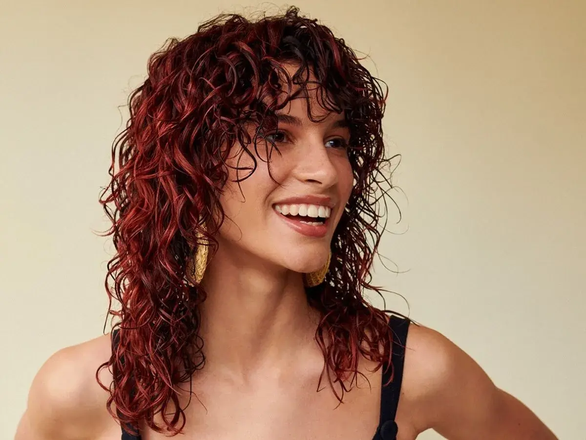 Donna sorridente con splendidi capelli mogano ricci e bagnati, che le incorniciano il viso.
