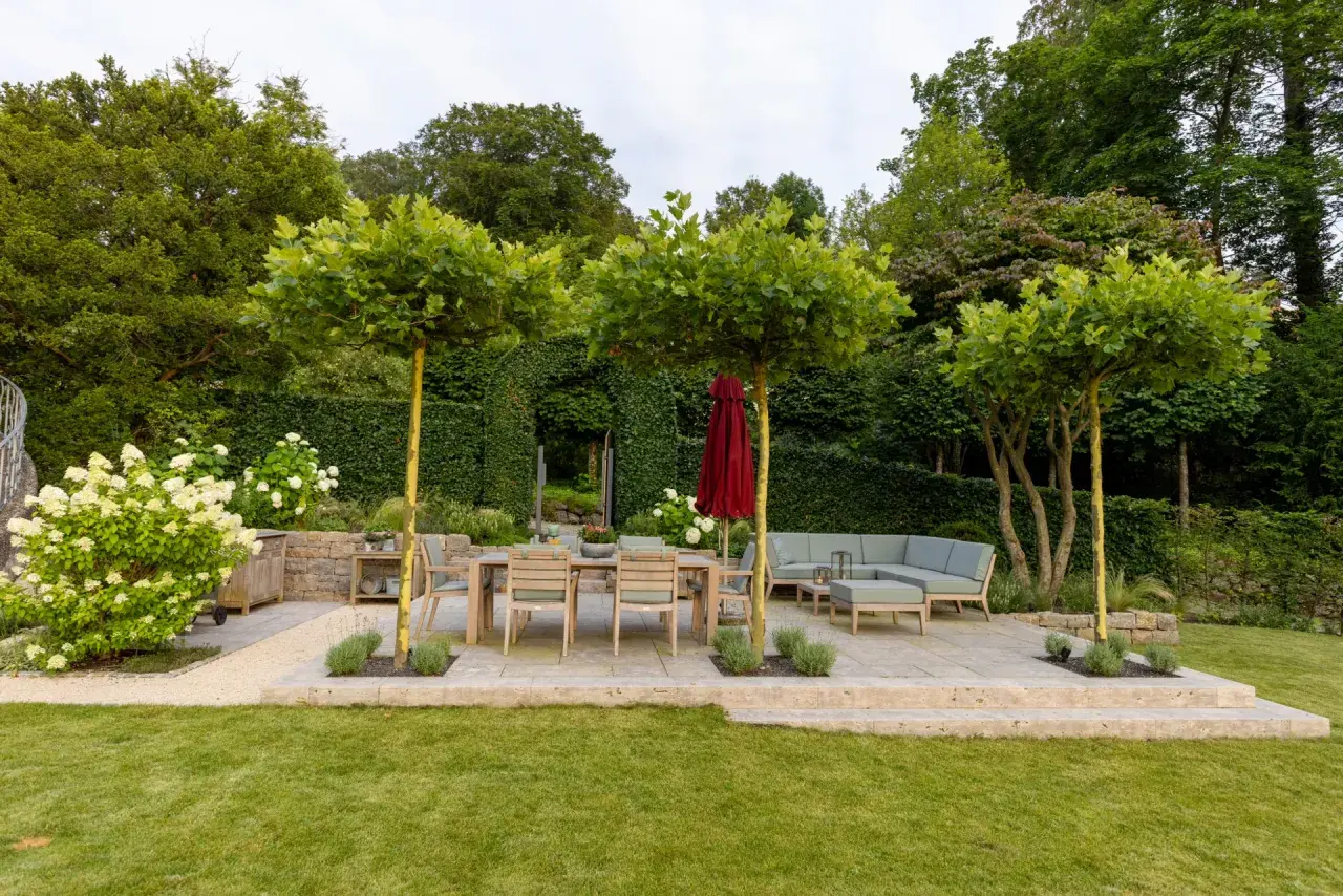 Ein gepflegter Garten mit einer hohen Hecke, die Privatsphäre schafft. Eine Terrasse mit Essbereich und Lounge lädt zum Verweilen ein.