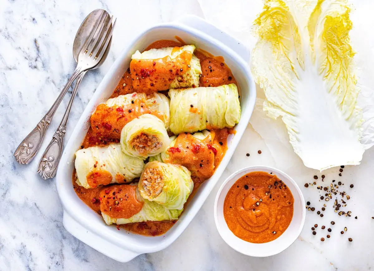 Pyszne gołąbki z kapusty pekińskiej w sosie, gotowe do podania. Obok liść kapusty i miseczka sosu.