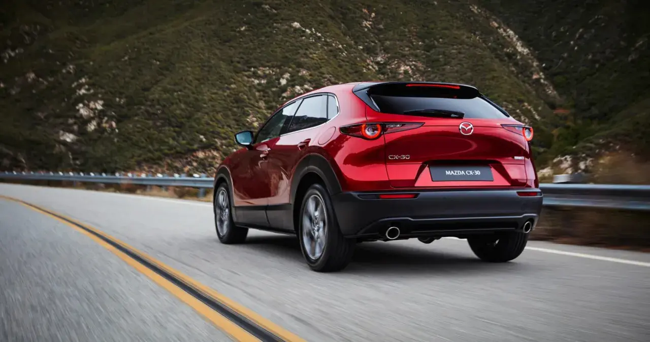 Röd Mazda CX-30 hybrid på en slingrig väg i bergen. Testkörning av den nya modellen.