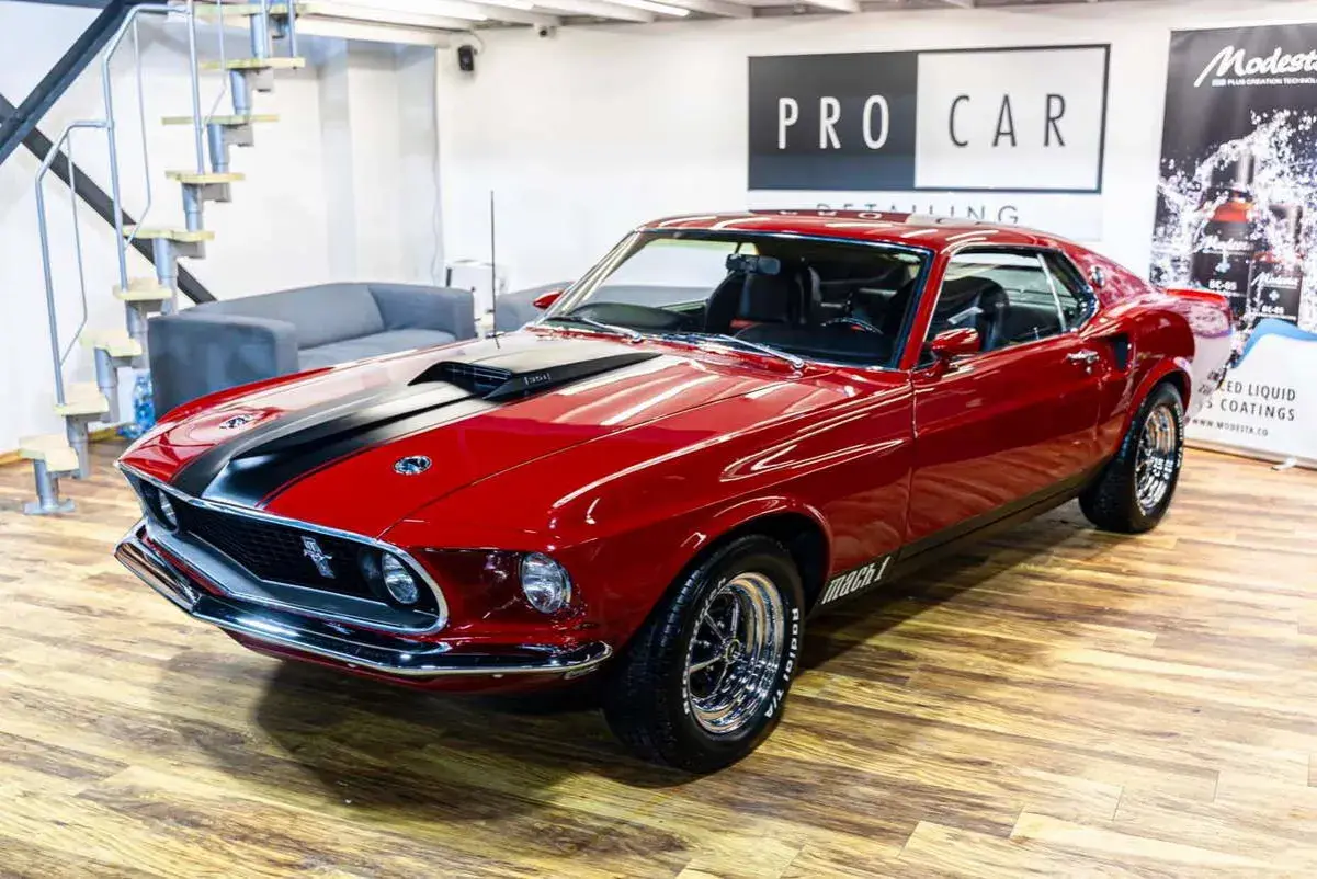 Błyszczący czerwony Ford Mustang Mach 1 z 1969 roku z czarnymi pasami na masce, gotowy do jazdy.