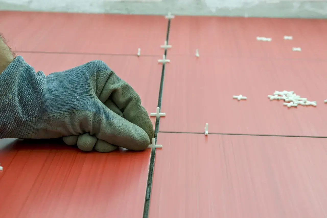 Main tenant, ganté, ajuste des croisillons pour refaire le joint du carrelage rouge.
