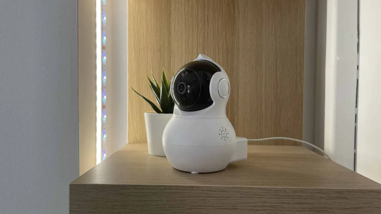 Cámara de vigilancia blanca con lente negra, parte de un sistema domótico, junto a una planta y luces LED.