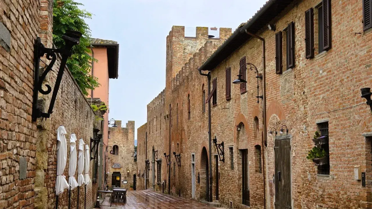 Vicoli medievali di Certaldo cosa vedere: un'antica strada in mattoni con torri merlate, lampioni in ferro battuto e finestre con persiane.