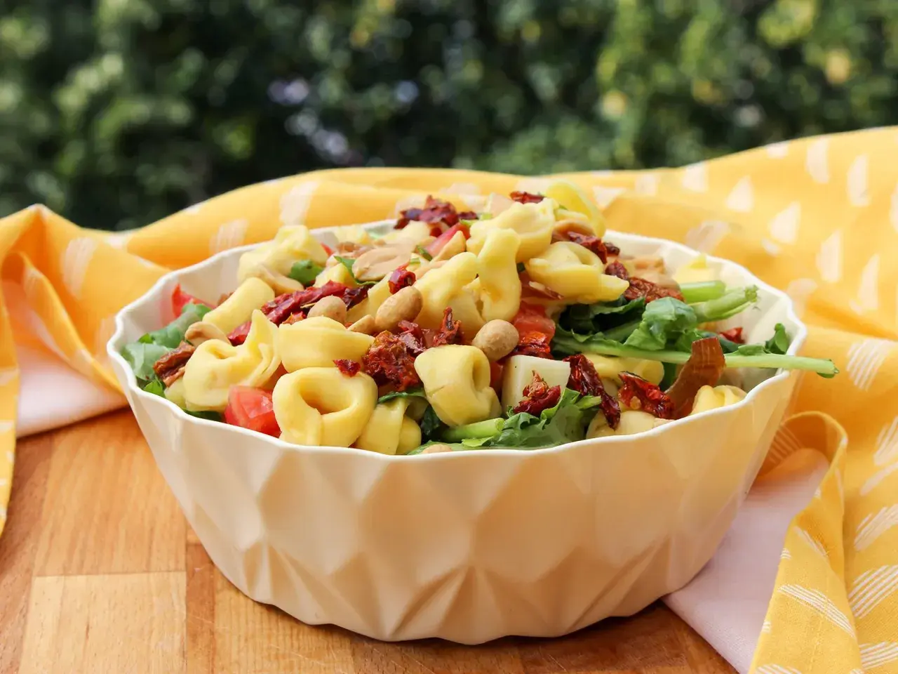 Ein köstlicher tortellini salat mediterran mit sonnengetrockneten Tomaten und Nüssen, serviert in einer weißen Schüssel auf einem Holztisch.
