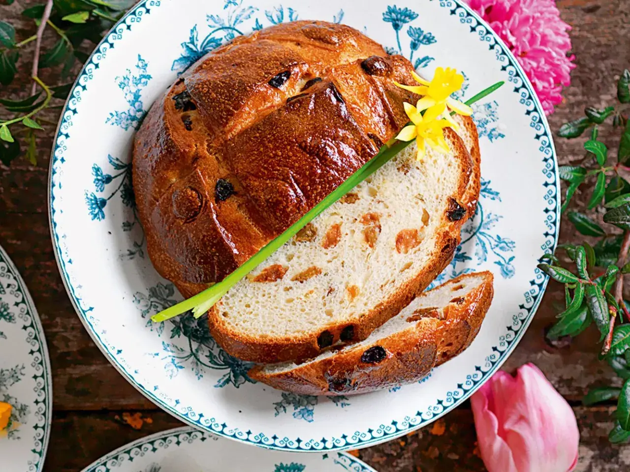 Pan di ramerino dorato, con uvetta e scorze candite, guarnito con un fiore giallo e un rametto verde.