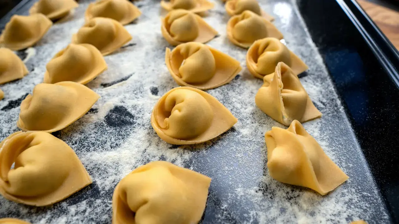 Frisch geformte Tortellini liegen auf einer bemehlten Fläche. Das Selbermachen von Tortellini ist ein Genuss für alle Sinne.