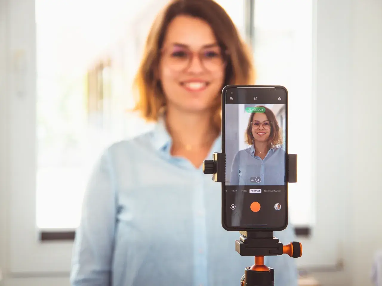 Frau macht ein bewerbungsfoto selber machen mit dem Handy auf einem Stativ.