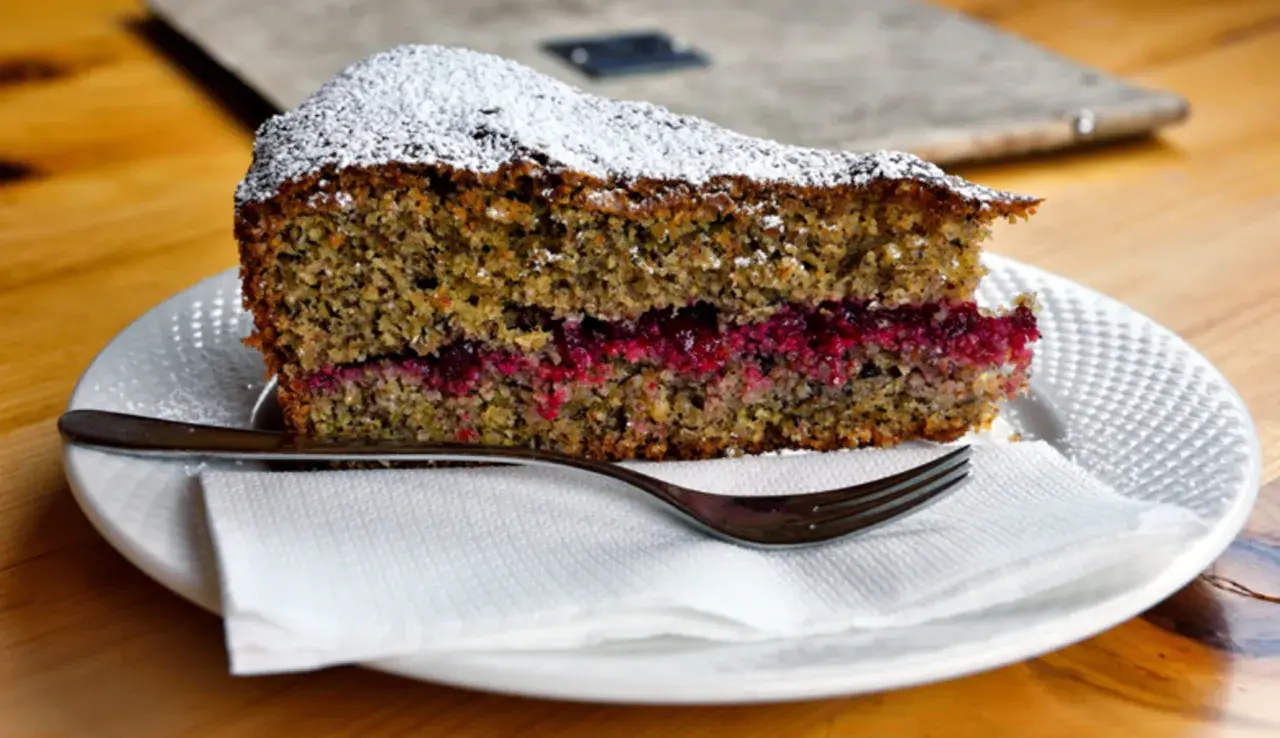 Una fetta di torta con farina di grano saraceno e cioccolato, farcita con marmellata di frutti rossi, spolverata di zucchero a velo.