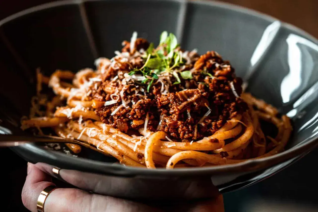 Ein Teller Spaghetti Ragu, garniert mit Parmesan und frischen Kräutern, wartet darauf, genossen zu werden.