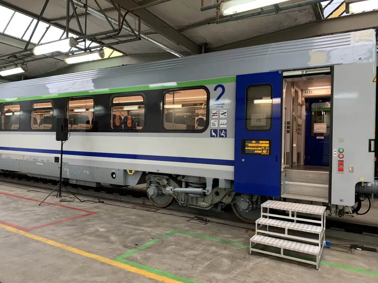 Wagon 175a w hali serwisowej, z otwartymi drzwiami i schodkami. Widać wnętrze z siedzeniami i numer wagonu "2".