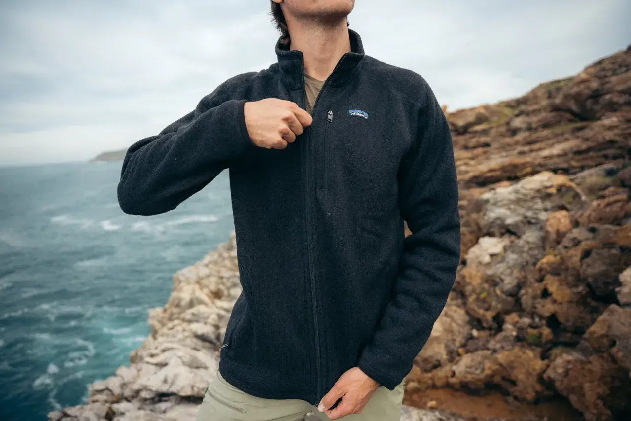 A man zips up a dark grey sweater fleece jacket, perfect for a coastal adventure. The textured fabric offers warmth and comfort.