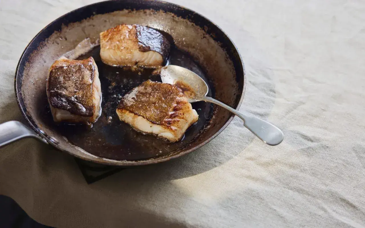 Stekta koljabit i en panna, redo för ett enkelt kolja recept. En sked ligger bredvid.