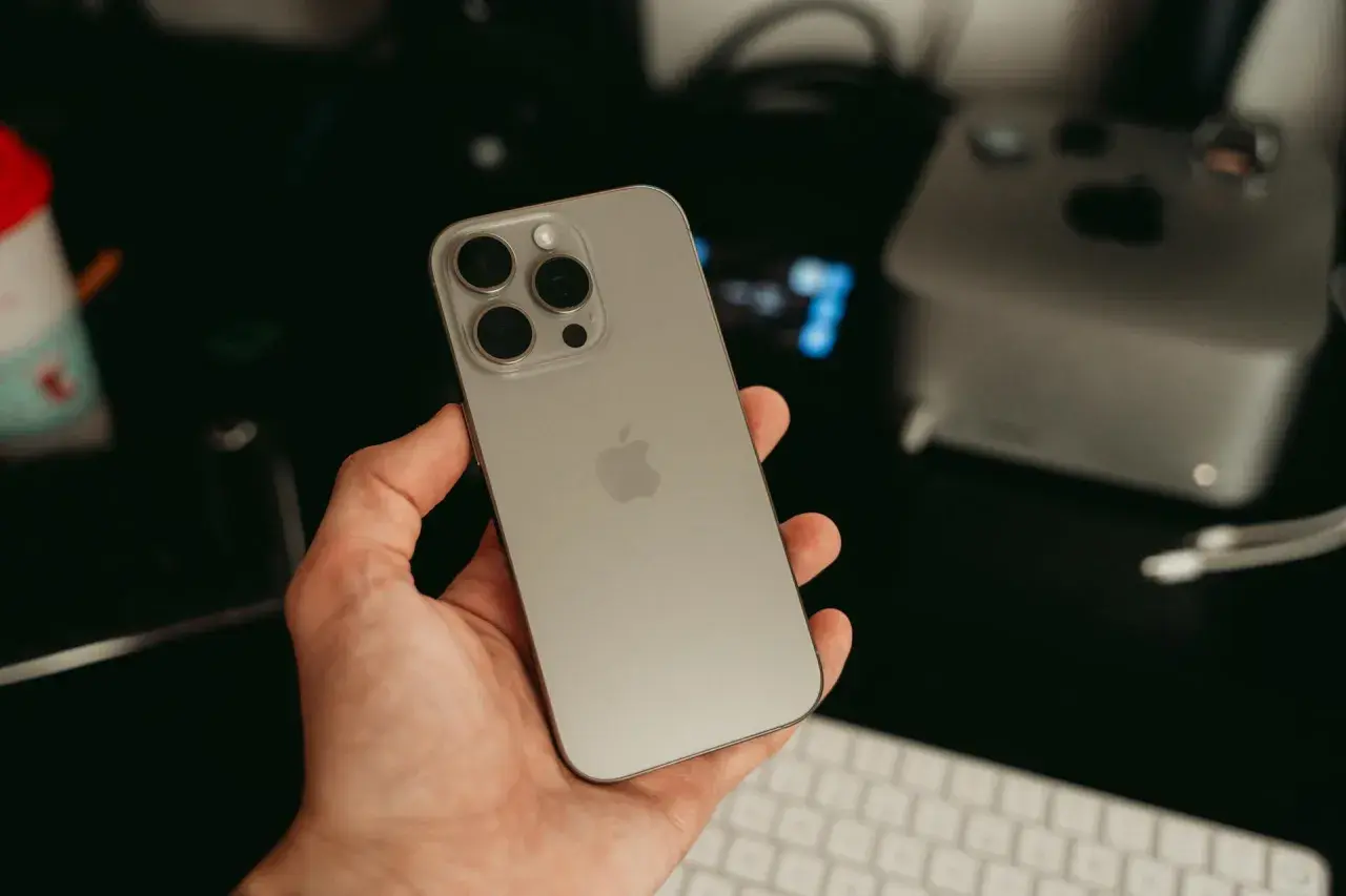 Dłoń trzyma nowy iPhone 16 ultramaryna. Z tyłu widoczny moduł aparatów i logo Apple.