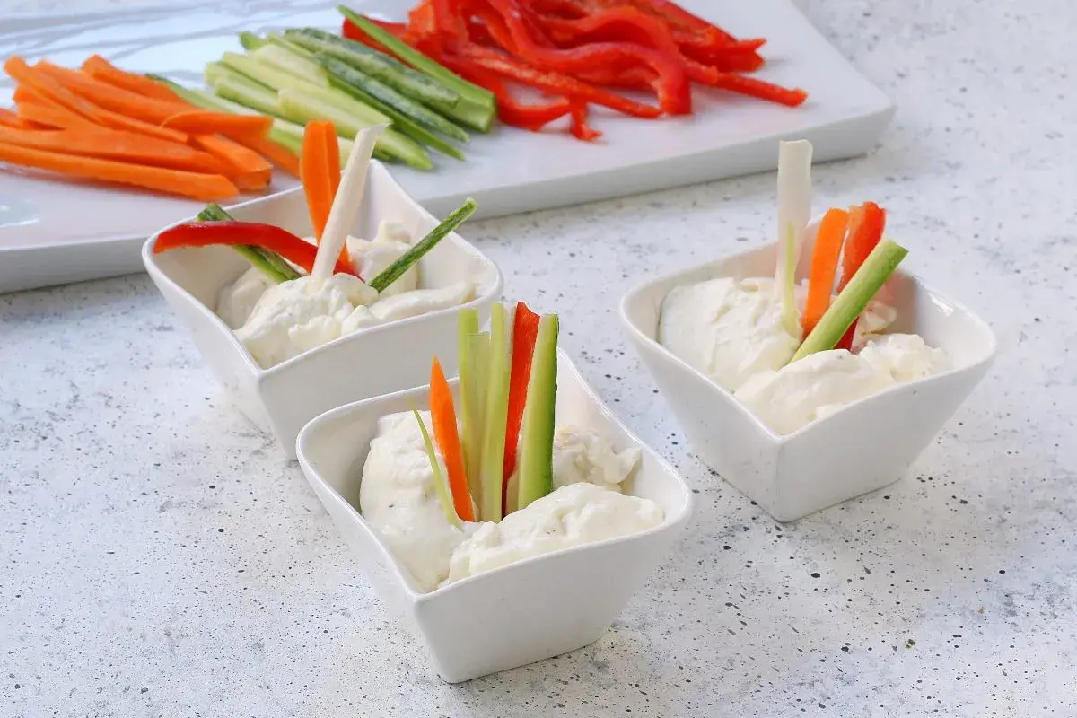 Tre ciotoline con mousse di caprino e bastoncini di verdure fresche: carote, cetrioli e peperoni rossi.