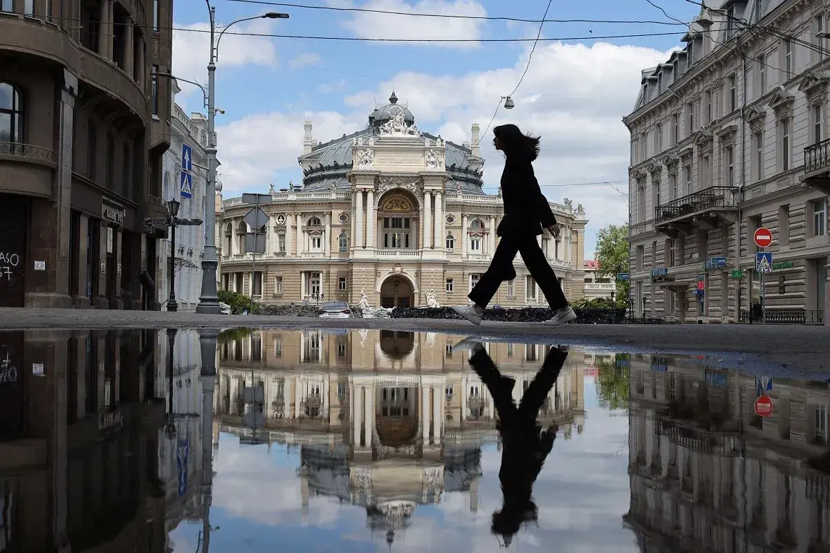 Kobieta idzie przez kałużę przed Teatrem Opery i Baletu w Odessie, tworząc odbicie niczym z filmu.