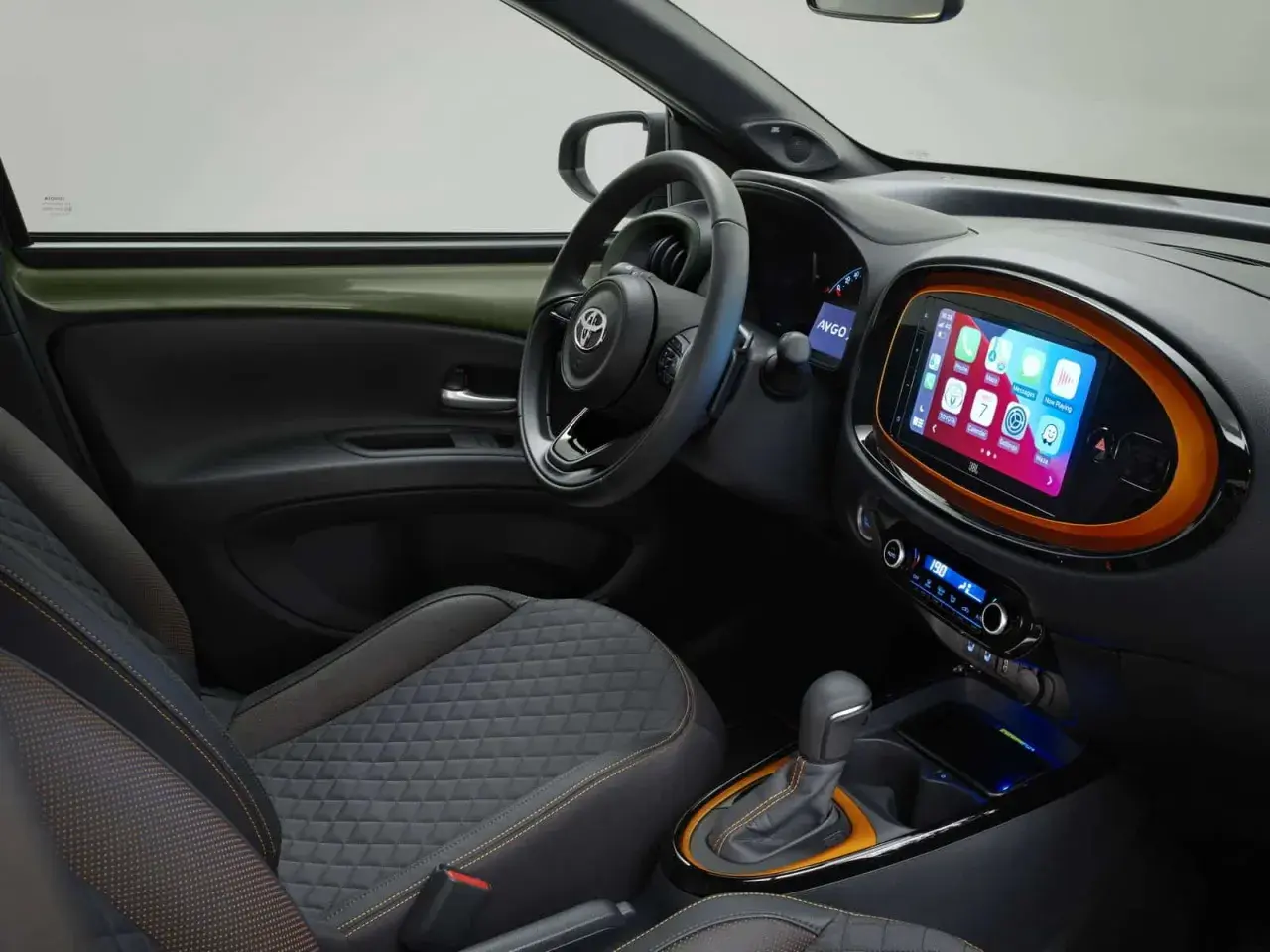 Interni moderni della Toyota Aygo X: sedili trapuntati, volante sportivo e un vivace touchscreen centrale con Apple CarPlay.