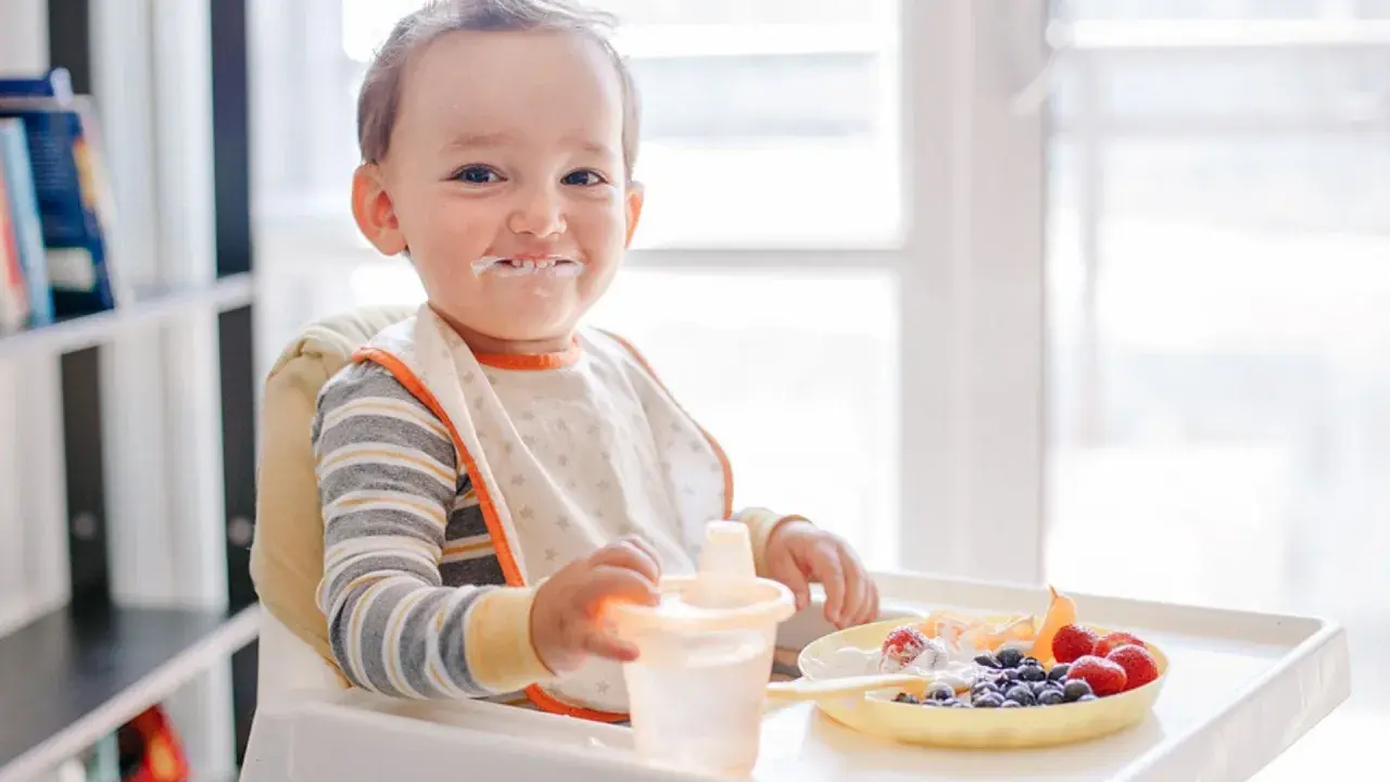 Kleiner Junge mit Heidelbeeren und Joghurt im Gesicht, der an seinem Becher nippt.