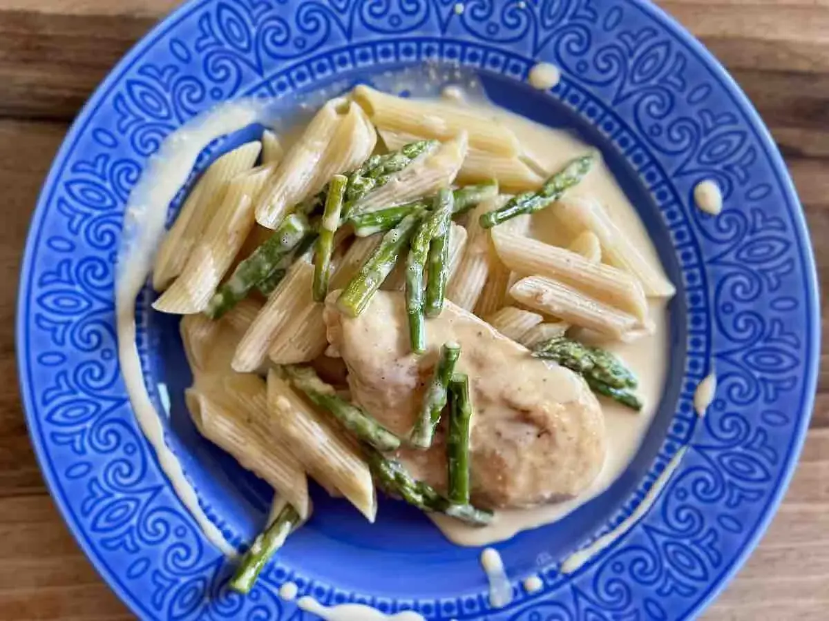 Penne z piersią kurczaka i szparagami w kremowym sosie, podane na niebieskim talerzu.
