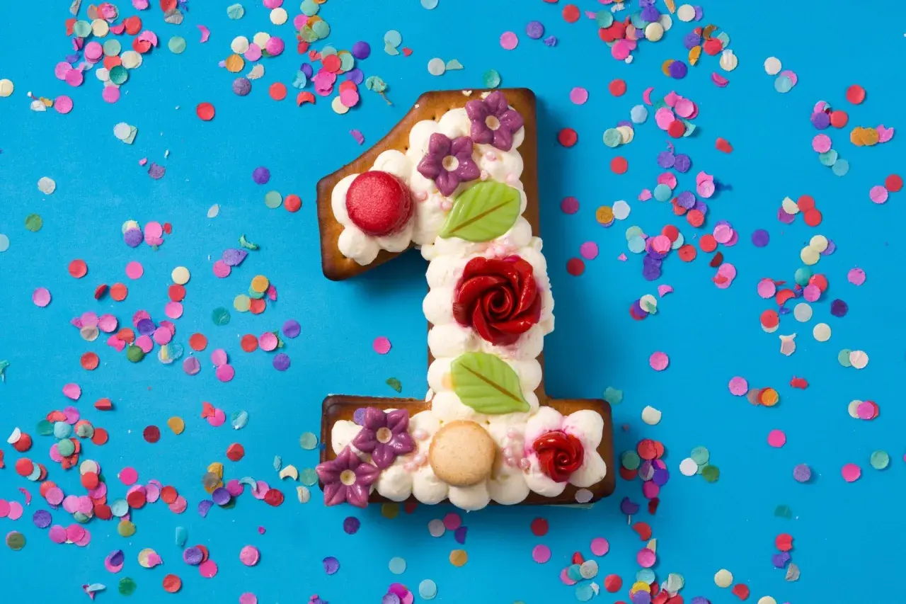 Ein süßer number cake in Form einer Eins, verziert mit Sahne, Blumen und Rosen, umgeben von buntem Konfetti.