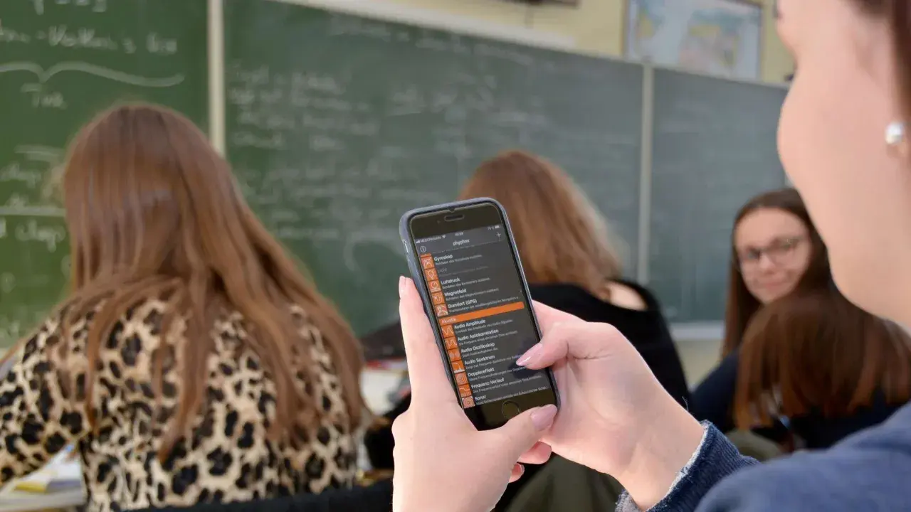 Schülerinnen nutzen Smartphones im Unterricht für physikalische Experimente. Eine App zeigt Messwerte von Gyroskop, Luftdruck und Akustik.