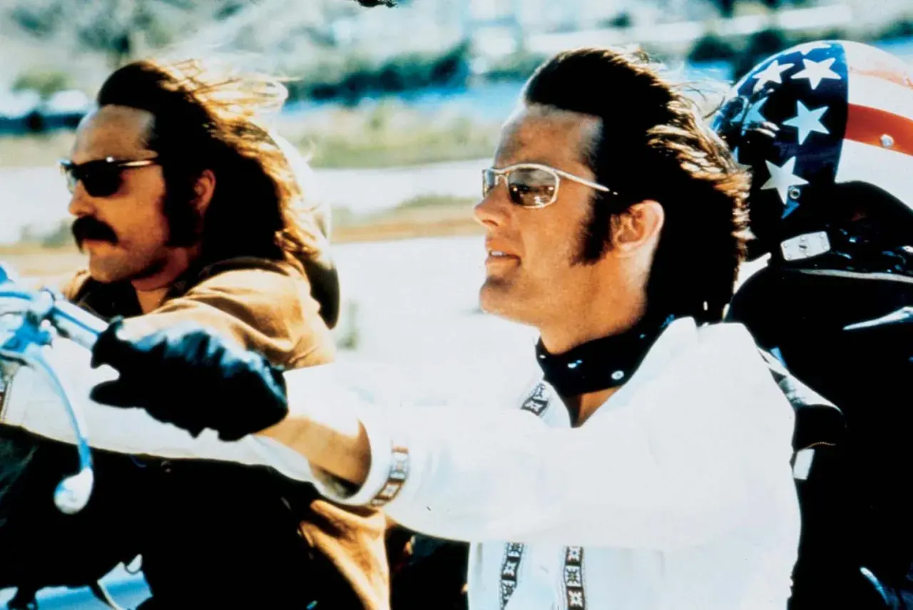 Wycieczka z rollistan i Easy Rider. Dwóch motocyklistów w okularach przeciwsłonecznych i skórzanych rękawiczkach jedzie na motocyklu.
