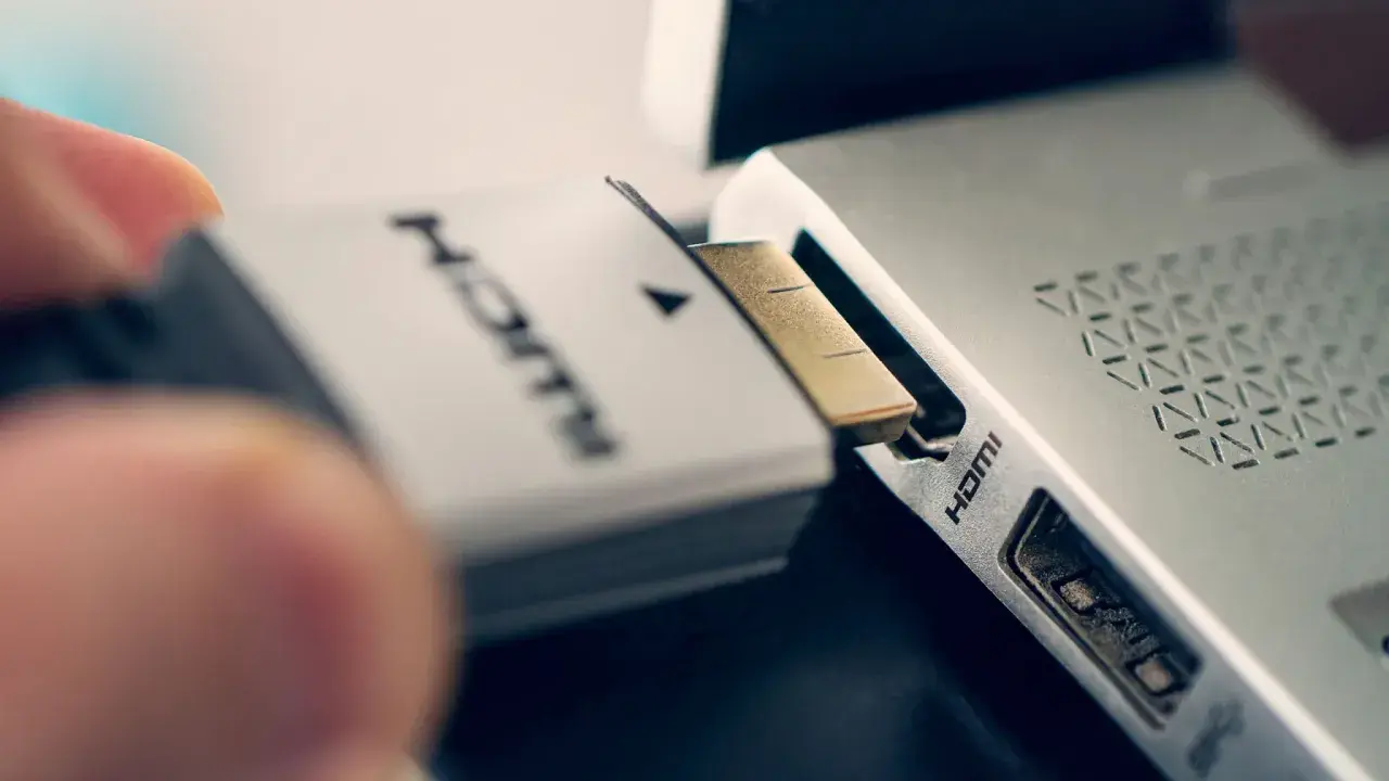 Ein Finger steckt ein HDMI-Kabel in den HDMI-Anschluss eines Laptops.