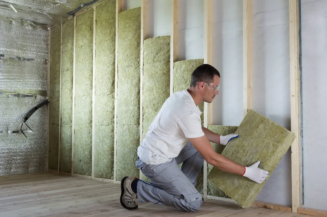 Un ouvrier installe un panneau d'isolant thermique dans une structure murale en bois.