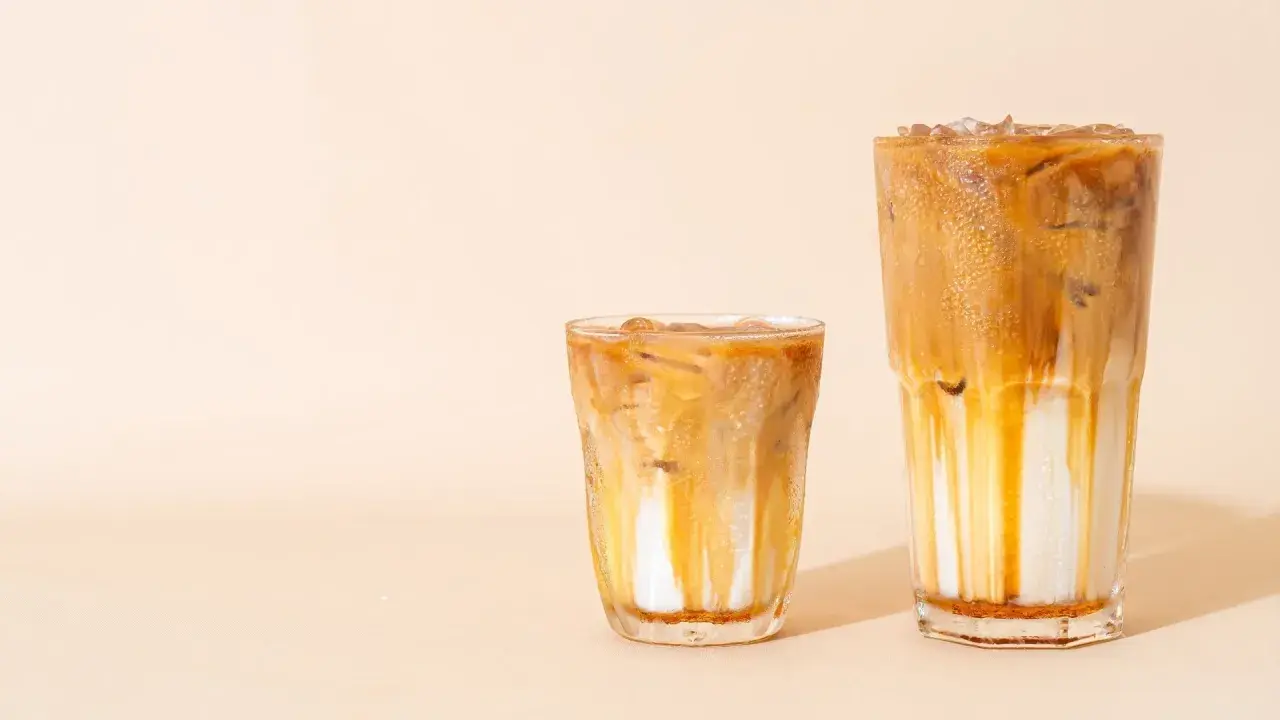 Zwei Eiskaffees: Ein kleinerer, der an einen Cappuccino erinnert, und ein größerer, der wie ein Latte Macchiato aussieht, mit Eis und Karamellsauce.