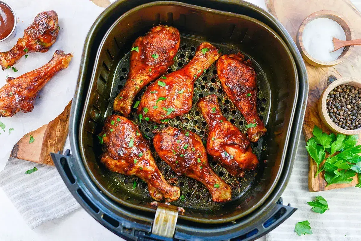 Soczyste udka z kurczaka z airfryer, polane sosem barbecue i posypane natką pietruszki. Obok miseczki z solą i pieprzem.