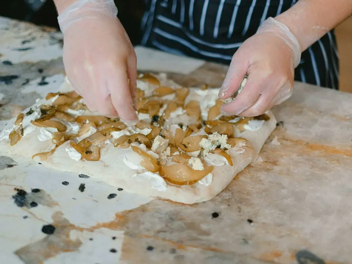 Manos enguantadas añaden queso azul a una focaccia con peras. Una deliciosa focaccia reteta en proceso.