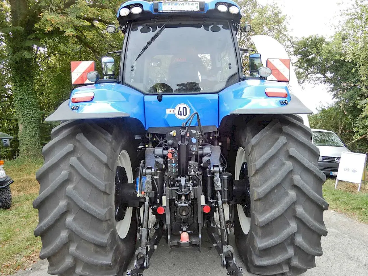 Blauer Traktor mit großen Reifen. An der Seite sind rot-weiße Warnschilder mit Beleuchtung angebracht.